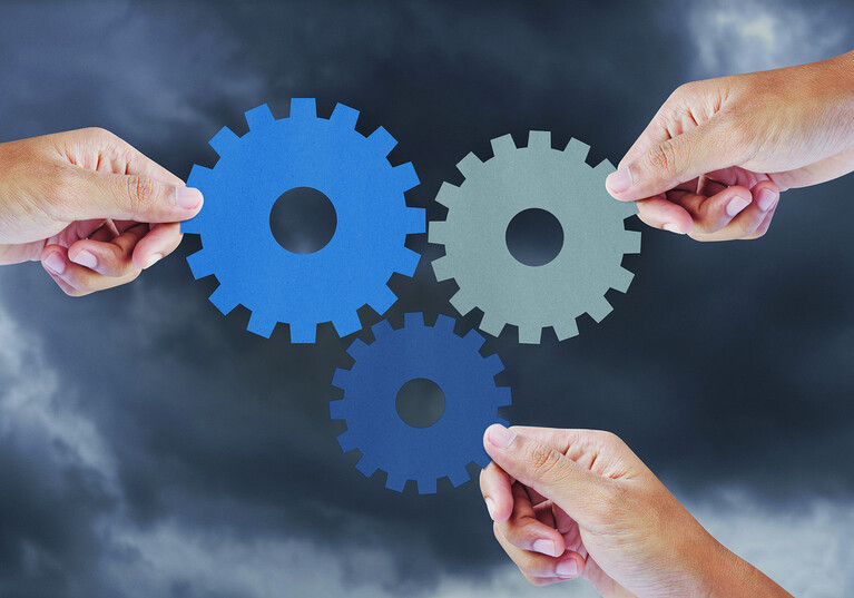 Hand show gear to teamwork as concept in storm clouds